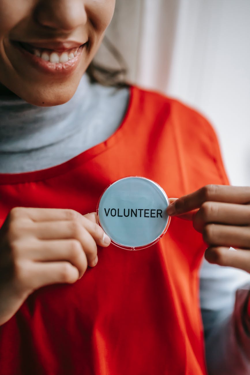 smiling ethnic woman showing volunteer sign on red apron